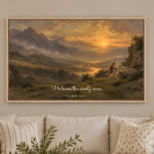May include: A rectangular landscape wall art print in a light wood frame featuring a sunset over mountains and a valley. The text "He leaves the ninety-nine" and "LUKE 15:4" is printed in white script and serif font in the lower center of the artwork.