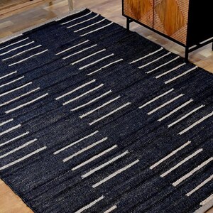 May include: A rectangular area rug featuring a dark black base color with a repeating pattern of short, horizontal, off-white dashed lines arranged in staggered vertical columns across the entire surface of the woven floor covering.