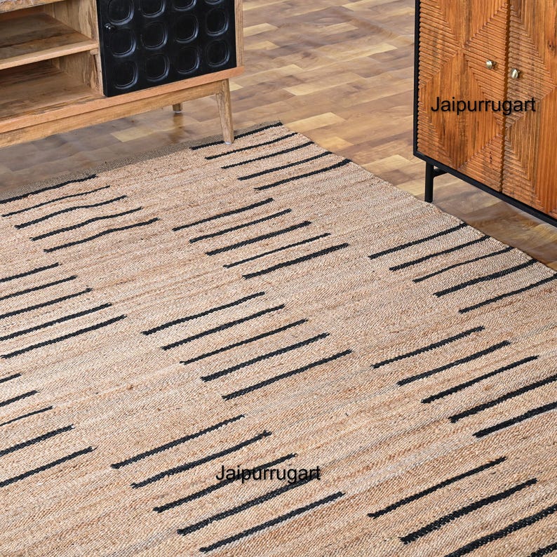 May include: A natural fiber rug with a geometric pattern of black stripes on a beige background. The rug is made of jute and is perfect for adding a touch of natural texture to any room.