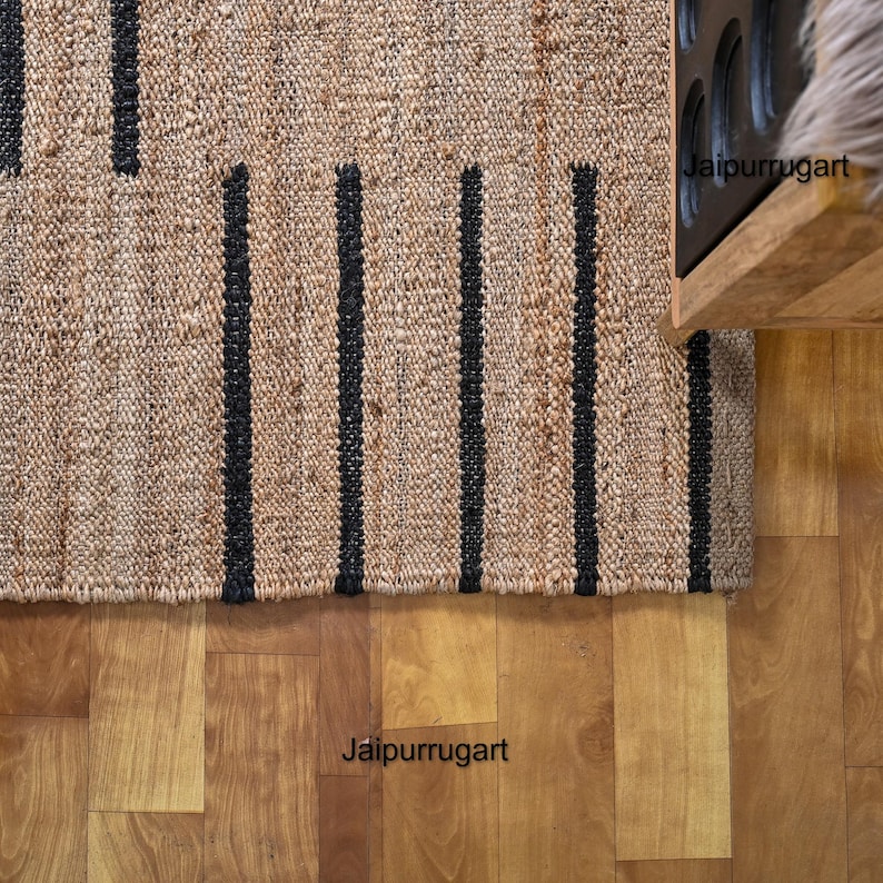 May include: A natural fiber rug with black stripes. The rug is made of jute and has a natural, earthy look. The rug is shown on a wooden floor.