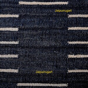May include: A dark navy blue woven textile featuring a repeating pattern of horizontal cream-colored stripes. The fabric has a visible coarse texture with a grid-like weave. The yellow text Jaipurrugart is printed twice on the surface of the fabric.
