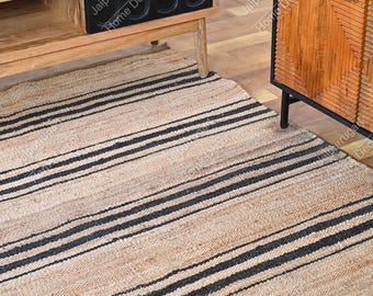 May include: A rectangular area rug featuring a natural tan jute fiber base with repeating horizontal black stripes. The rug is positioned on a wooden floor beneath a wooden media console with black cabinet doors and a wooden cabinet with a textured front.