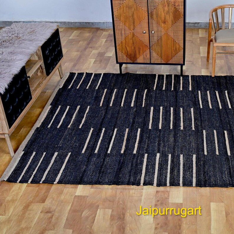 May include: A rectangular area rug featuring a dark black base with a repeating pattern of short, vertical, light beige stripes arranged in staggered columns. The rug is positioned on a light-colored wooden floor, with the text Jaipurrugart visible.
