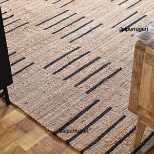 May include: A natural fiber rug with a geometric pattern of black lines on a beige background. The rug is made of jute and is perfect for adding a touch of natural texture to any room.