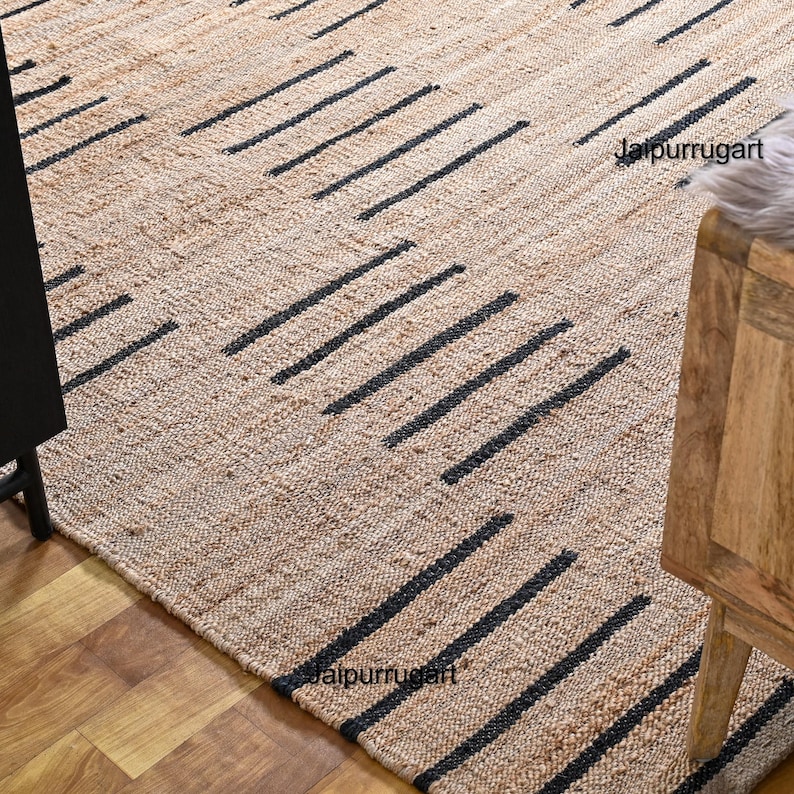 May include: A natural fiber rug with a geometric pattern of black lines on a beige background. The rug is made of jute and is perfect for adding a touch of natural texture to any room.