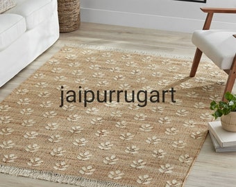 May include: A natural fiber rug with a cream and brown floral pattern. The rug has a fringe border and is made of jute. The rug is called "jaipurrugart".