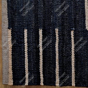 May include: A woven area rug featuring a dark navy blue base with vertical stripes in a natural beige tone. The texture appears coarse and fibrous, with a repeating pattern of dark panels separated by light-colored, raised vertical woven lines.