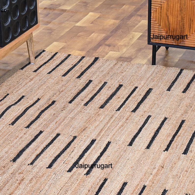 May include: A natural fiber rug with a geometric pattern of black stripes on a beige background. The rug is made of jute and is perfect for adding a touch of natural texture to any room. The rug is shown in a home setting with wooden furniture.