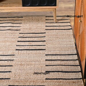 May include: A natural fiber rug with a black and beige striped pattern. The rug is made of jute and has a natural, earthy look. The rug is perfect for adding a touch of rustic charm to any room.