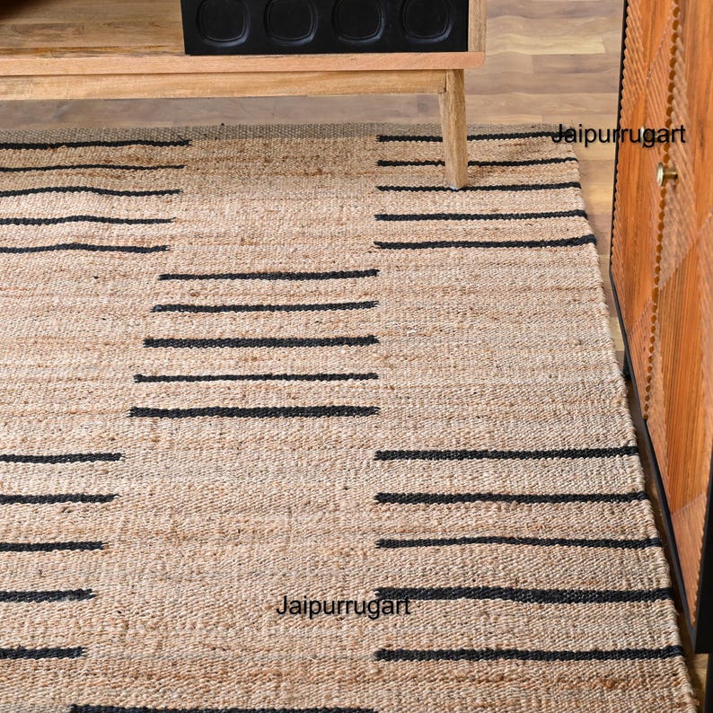 May include: A natural fiber rug with a black and beige striped pattern. The rug is made of jute and has a natural, earthy look. The rug is perfect for adding a touch of rustic charm to any room.