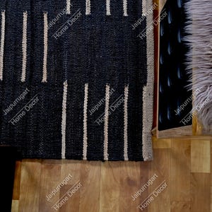 May include: A rectangular area rug featuring a woven black base with vertical beige stripes. The rug has a textured, natural fiber appearance with a consistent pattern of repeating lines across the surface, creating a high-contrast visual design.