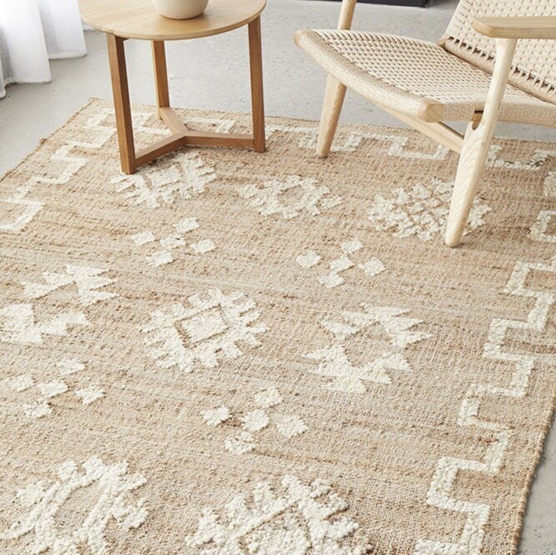 May include: A natural fiber rug with a geometric pattern in a light beige color. The rug has a woven texture and features a white design.
