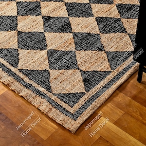 Op de afbeelding: Zwart en tan jute vloerkleed met ruitpatroon en een zwarte rand. Het vloerkleed is gemaakt van natuurlijke vezels en heeft een rustieke uitstraling.