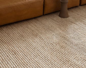 May include: A close-up of a natural fiber rug with a woven texture. The rug is a light beige color and has a subtle pattern.