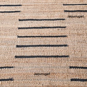 May include: A natural fiber rug with a geometric pattern of black stripes on a beige background. The rug is made of jute and is a natural, sustainable material. The rug is perfect for adding a touch of natural beauty to any room.