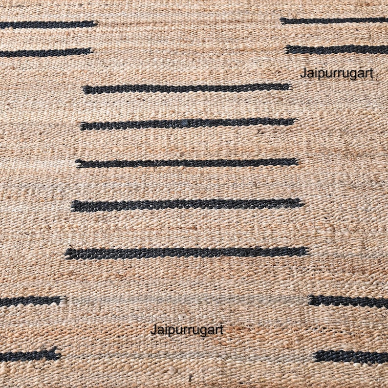 May include: A natural fiber rug with a geometric pattern of black stripes on a beige background. The rug is made of jute and is a natural, sustainable material. The rug is perfect for adding a touch of natural beauty to any room.