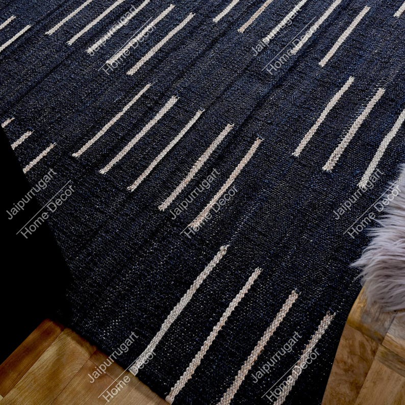 May include: A dark navy blue area rug featuring a repeating pattern of short, vertical, off-white dashed lines arranged in staggered rows across the textured surface. The rug has a woven appearance with visible fibers and a consistent geometric design.