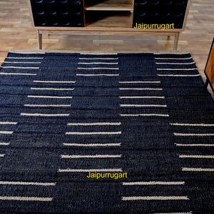 May include: A rectangular area rug featuring a dark navy blue base with a repeating geometric pattern of horizontal cream-colored stripes. The rug has a textured, woven appearance and includes the text Jaipurrugart in yellow on the surface.