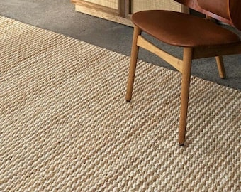 May include: A natural fiber rug with a woven texture in a light brown color. A wooden chair with a brown leather seat is sitting on the rug.