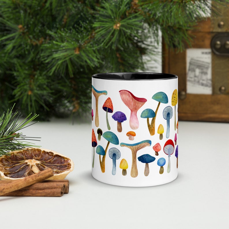 May include: White ceramic mug with a black rim and handle. The mug features a colorful watercolor illustration of various mushrooms.