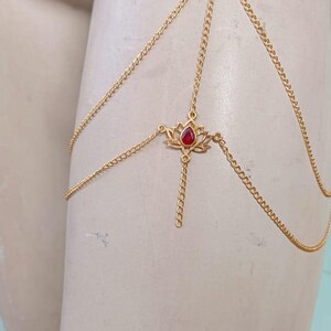 May include: Gold chain body jewellery with a red gem lotus flower pendant.