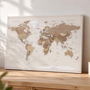 Könnte beinhalten: Eine gerahmte Weltkarte in Braun- und Beigetönen, mit detaillierten geografischen Merkmalen und Ländernamen. Die Karte liegt auf einer Holzoberfläche, mit dem Text "Emily & Oliver" in der linken unteren Ecke.