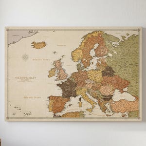 May include: A rectangular wall map of Europe featuring a vintage-inspired aesthetic with muted earth tones including shades of brown, tan, and olive green. The map displays geographical borders, labeled countries, and the text EUROPE MAP TRAVELS.