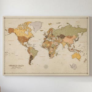 May include: A rectangular wall art print featuring a world map with a vintage aesthetic. The map displays continents in muted shades of tan, brown, and olive green against a cream background. Text in the lower left corner reads WORLD MAP OUR TRAVELS.