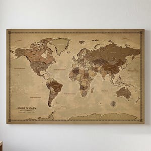 May include: A rectangular world map wall art piece featuring a vintage-inspired sepia and brown color palette. The map displays continents and oceans with detailed borders and includes the text "WORLD MAP" and "OUR TRAVELS" in the lower left corner.