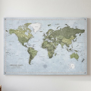 May include: A framed world map with a light blue background and green landmasses. The map includes the text "WORLD MAP" and is surrounded by a decorative border. The map is hanging on a white wall.