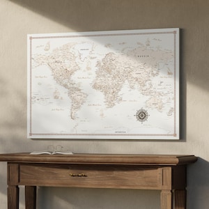 Peut inclure: Une carte du monde blanche avec du texte et des lignes marrons. La carte est encadrée et accrochée à un mur au-dessus d'une table en bois.