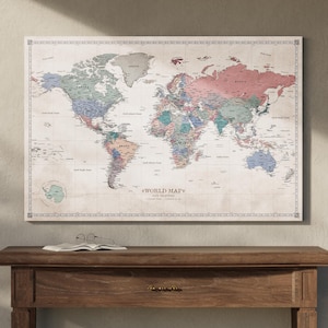 May include: A large world map canvas print with a vintage aesthetic, featuring a detailed depiction of continents and countries in various colors. The map is mounted above a wooden table with a book and glasses.