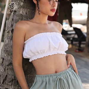 Puede incluir: Un top blanco sin tirantes con un escote con volantes y un pantalón verde claro con cordón.