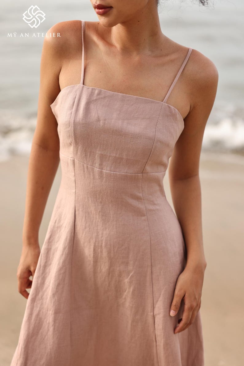 Close-up front shot focusing on the bodice of a dusty pink linen dress, highlighting the straight neckline, thin shoulder straps, and structured panel stitching.
