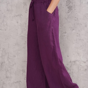 Three-quarter front full-body view of the model posing with her hand in her pocket against the studio wall, highlighting the casual chic elegance of the purple linen ensemble.