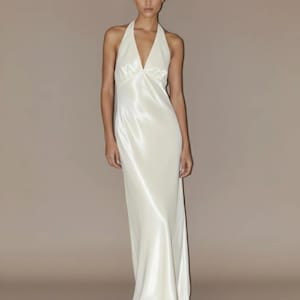 May include: An ivory-coloured, floor-length halter dress. The dress has a deep V-neck and is made of a flowing, silky fabric. It is sleeveless and has a simple, elegant design, suitable for formal events.