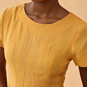 Close-up front view focusing on the upper bodice and round neckline of a mustard yellow linen dress, highlighting the delicate fine vertical stitching details on the chest.