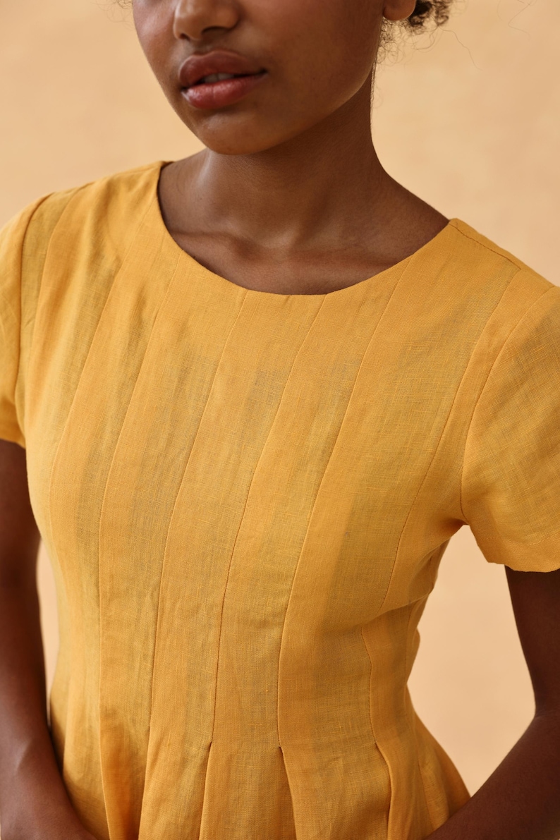 Close-up front view focusing on the upper bodice and round neckline of a mustard yellow linen dress, highlighting the delicate fine vertical stitching details on the chest.