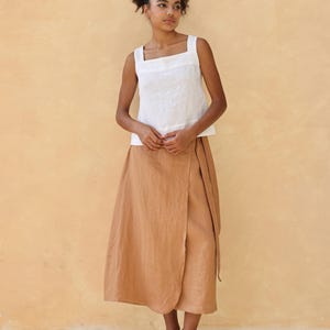 A full-length front-facing shot of the model standing straight against the beige studio wall. The minimalist pose summarizes the classic look, showing how the square neckline and wide sleeveless straps create a balanced, modern aesthetic.