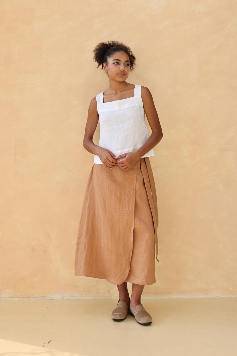 A full-length front-facing shot of the model standing straight against the beige studio wall. The minimalist pose summarizes the classic look, showing how the square neckline and wide sleeveless straps create a balanced, modern aesthetic.