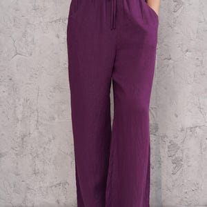 Front cropped view from the waist down focusing on the magenta purple trousers, highlighting the comfortable gathered elastic waist and relaxed drape over the feet.