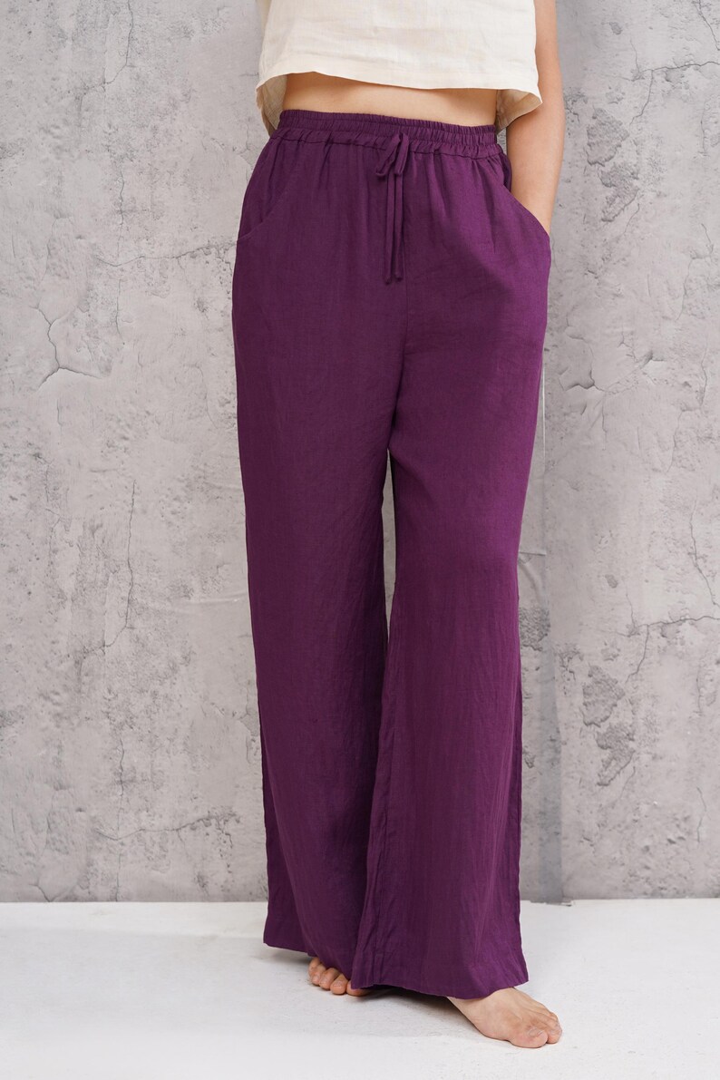 Front cropped view from the waist down focusing on the magenta purple trousers, highlighting the comfortable gathered elastic waist and relaxed drape over the feet.