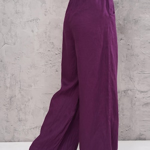 Rear three-quarter full-length shot of the model in the studio, showcasing the flattering back silhouette and dramatic wide-leg hem of the magenta purple pants.