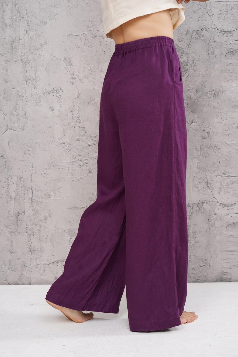 Rear three-quarter full-length shot of the model in the studio, showcasing the flattering back silhouette and dramatic wide-leg hem of the magenta purple pants.