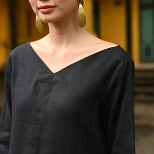 Medium close-up shot focusing on the upper half of the garment, highlighting the wide V-neckline design, relaxed shoulders, and natural texture of the black linen fabric.