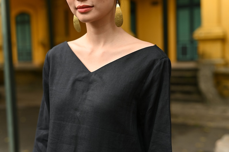 Medium close-up shot focusing on the upper half of the garment, highlighting the wide V-neckline design, relaxed shoulders, and natural texture of the black linen fabric.