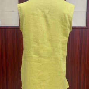 Back view of the chartreuse linen tunic on the dress mannequin, showcasing the simple high crew neckline at the back and the straight, relaxed-fit hemline.