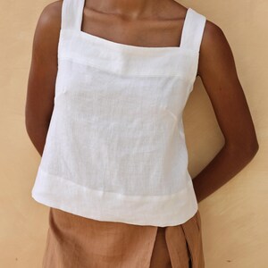 A tight close-up shot focusing on the upper bodice of the white linen top. The photo displays the clean-cut square neckline framing the chest and details the fine horizontal chest seam accenting the textured 200gsm pre-washed linen fabric.