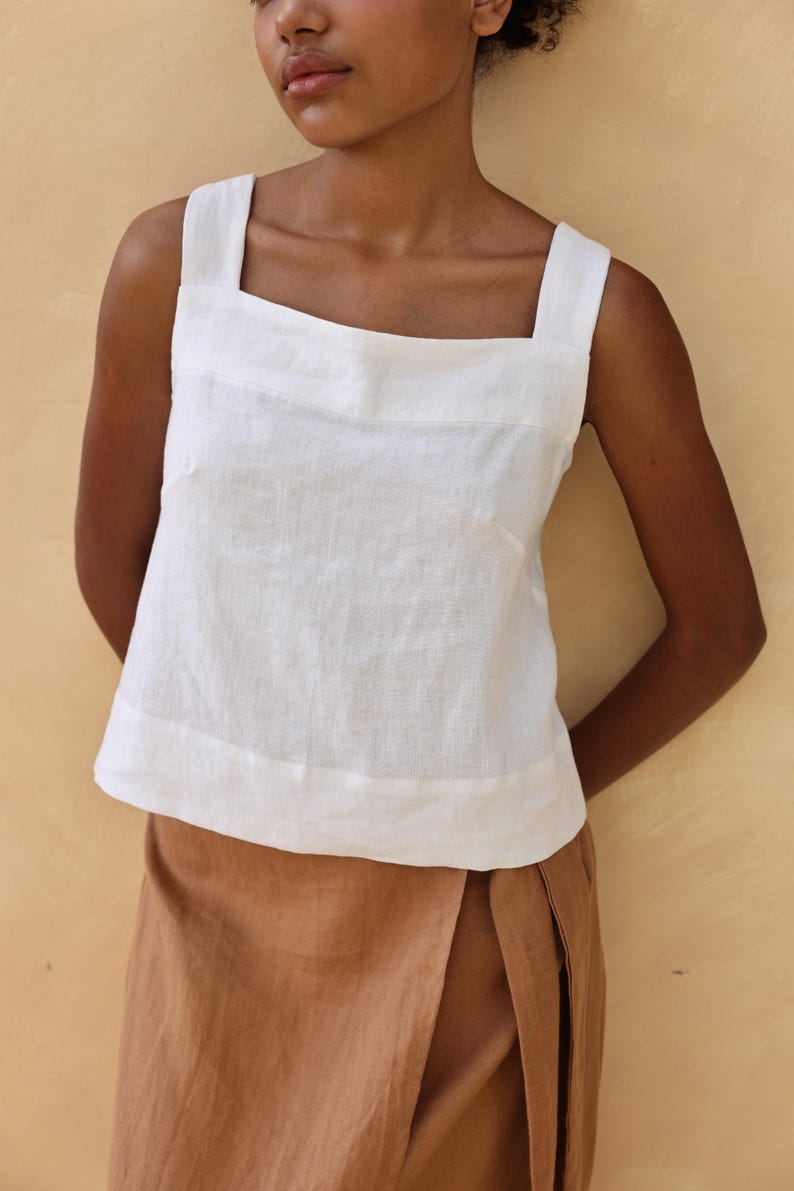 A tight close-up shot focusing on the upper bodice of the white linen top. The photo displays the clean-cut square neckline framing the chest and details the fine horizontal chest seam accenting the textured 200gsm pre-washed linen fabric.