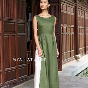 May include: A sleeveless, olive green maxi dress with a white panel on the side. The dress has a boat neckline and a fitted bodice that flows into a pleated skirt. The text "MYAN ATELIER" is visible.